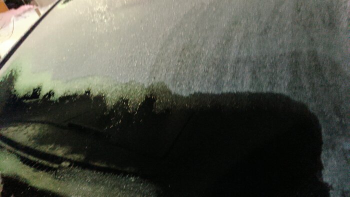 Avfrostat bilfönster delvis täckt med frost efter användning av kupévärmare och tomgångskörning.