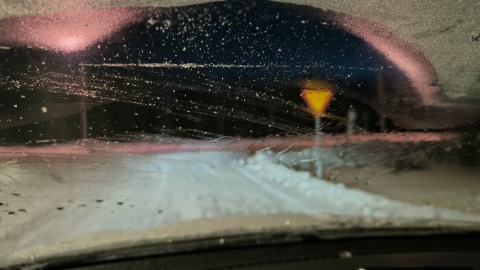 Bilruta med is och kondens från insidan trots användning av kupévärmare, snötäckt väg och trafikskylt synliga i bakgrunden.