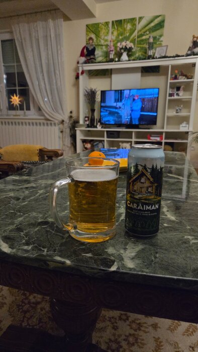 Ölglas och burk med Caraiman-öl på marmorbord, TV i bakgrunden.