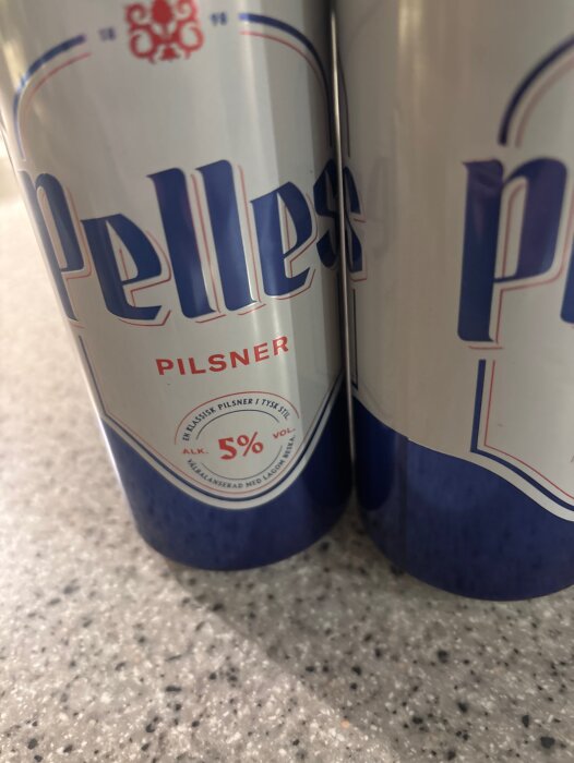 Burkar med Pelles pilsner, 5% alkoholhalt, står på en bänk.