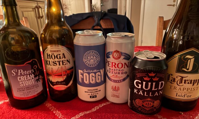 Flaskor och burkar med olika ölsorter uppställda på ett bord med röd duk.