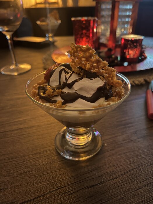 Ett glas dessert med chokladmousse, mintbaileyskräm, mandelflarnscrunch, maräng, jordgubbar och chokladsås på ett träbord.