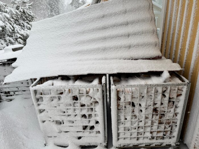 Snötäckt plåttak ovanpå vedförråd, tungt av snöfall, med snötyngda träd i bakgrunden.