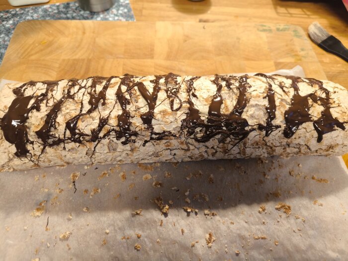 Hembakad stubbe dekorerad med smält choklad på bakplåtspapper, placerad på en träyta.