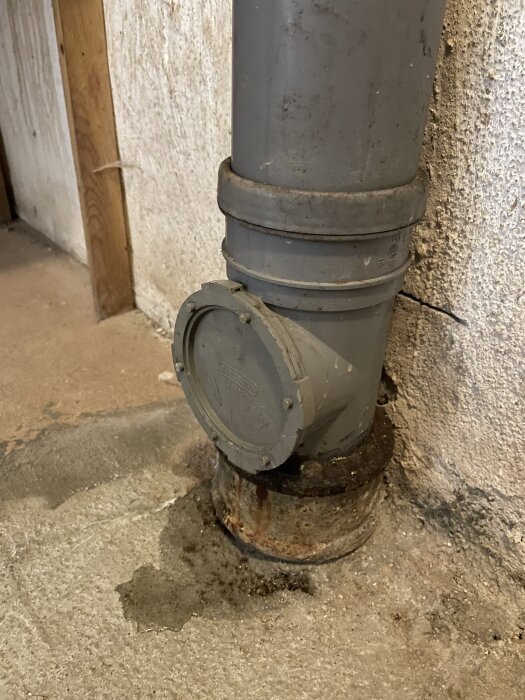 Inspektionslucka på avloppsrör med synlig läcka och vått golv under, del av problem efter rensning av rörstopp.
