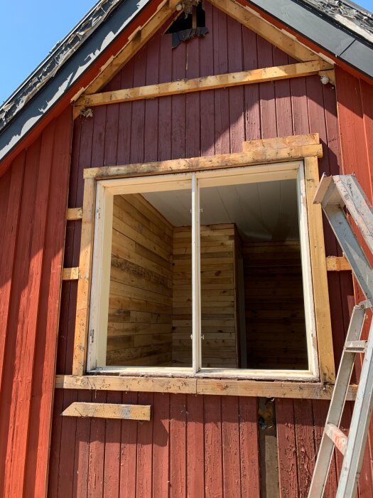 Renoverat rött hus med öppet fönster, synliga träväggar och en stege intill. Vindskivor och gammal fasad ses överst.