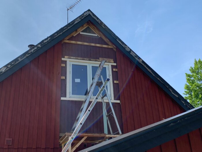 Gavel på rött hus med nyinstallerat fönster och stege. Originalfasad klädd med ny fasad. Vindskivor slitna och behöver bytas.