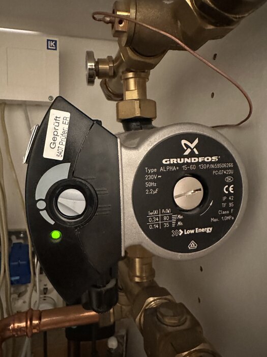 Cirkulationspump från Grundfos med serie ALPHA+. Grön indikatorlampa är tänd. Kopparrör och kopplingar är synliga runtomkring.
