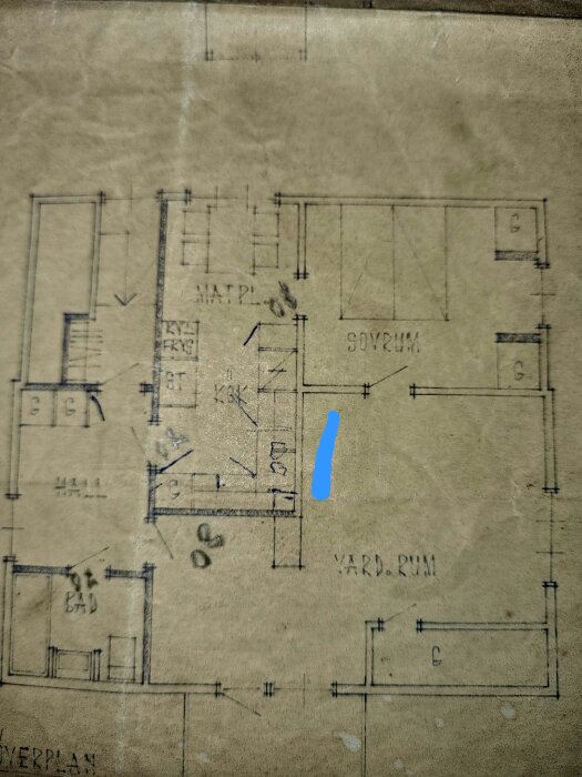 Planskiss med markerat blått streck nära köksområdet, visar möjlig bärande vägg bakom ventilationsrör. Rum markerade som matplats och vardagsrum.