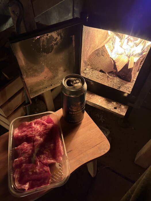 En bastu med öppen eld, en ölburk märkt "Norrsken" och en förpackning skivad chark på ett bord.