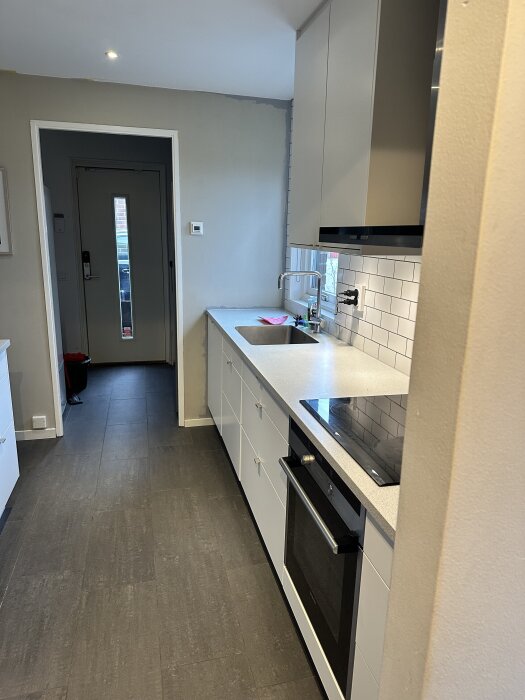 Kök med Marbodal inredning från 2015, inklusive spis och ugn, vit kaklad vägg, grått golv.