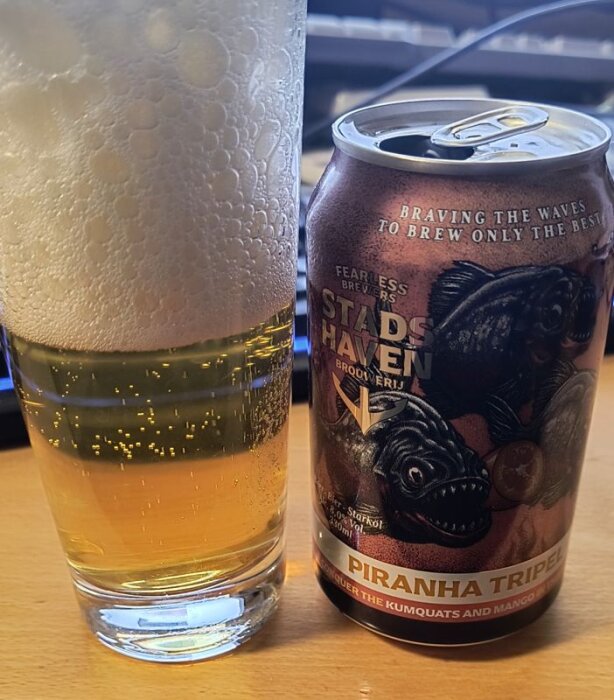 Ölglas med skum bredvid en burk Stadshaven Piranha Tripel, en starköl på 8%.