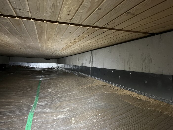 Bild av ett lågt ventilationsutrymme med träpanel i taket, plastfolie på marken och metallskivor på väggarna, tagen för att lösa ett problem.