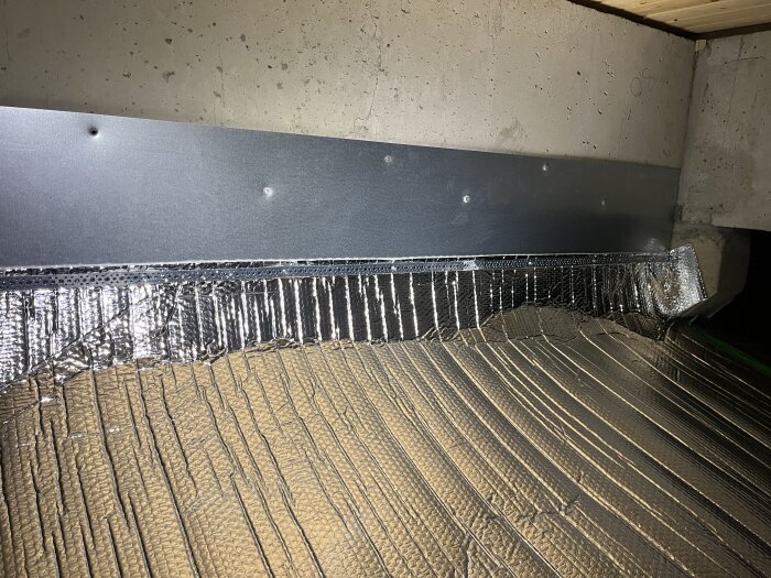 Isolering installerad på en vägg med reflekterande folie och metallpanel i en byggnadsstruktur.
