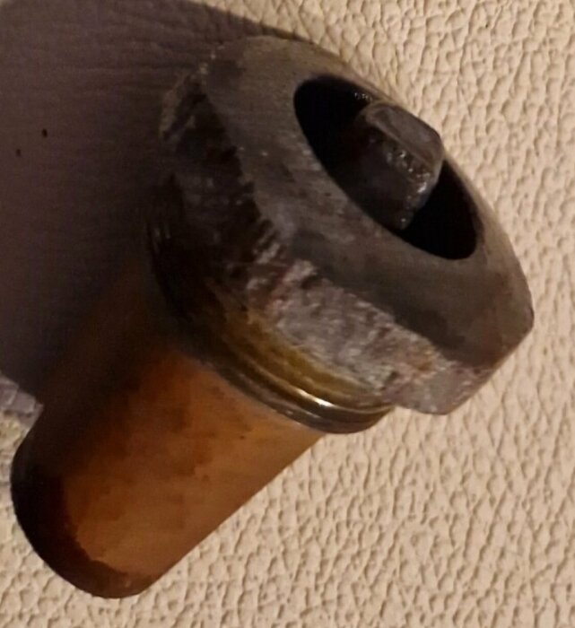 Rostig ventilkägla med avlägsnad ventilöverstycke på beige bakgrund.