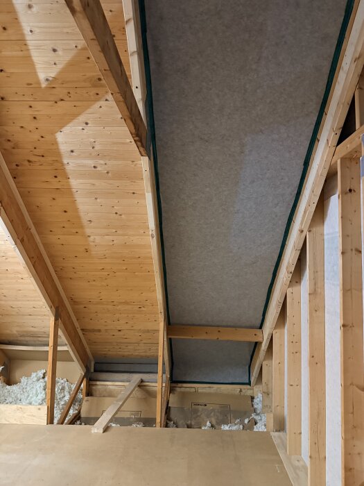 Träväggar och snedtak med synliga bjälkar och isoleringsmaterial på vinden under renovering för hemmabio.