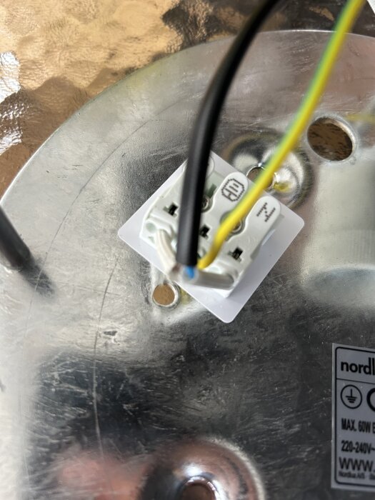 Anslutning av ytterlampa med blå, svart och gul-grön kablar mot metallisk bakgrund.