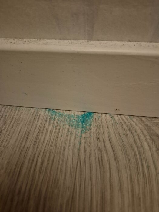 Blått pulver på golvet vid en vit golvlist.
