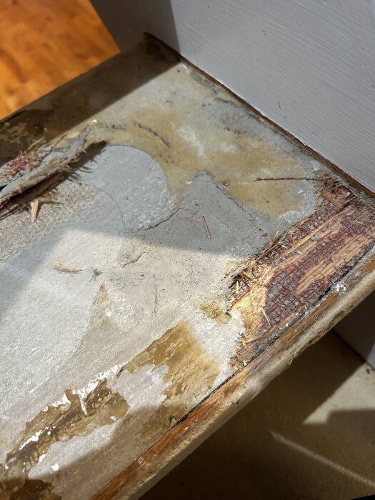 Sliten trappkant med borttaget matta och synliga limrester, med trä och linoleum i olika stadier av slitage och exponerade ytor.