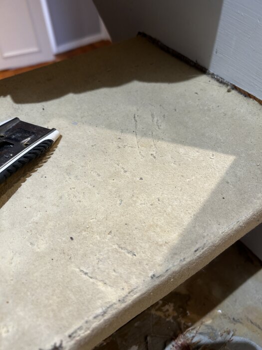 Steg i trä med gammalt lim och linoleum, sprickor synliga. Verktyg i hörnet, ljusinsläpp skapar skuggor. Trappan ska renoveras.