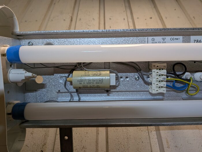 Interiör av lysrörsarmatur med LED-rör, synlig ballast och kopplingsplint.