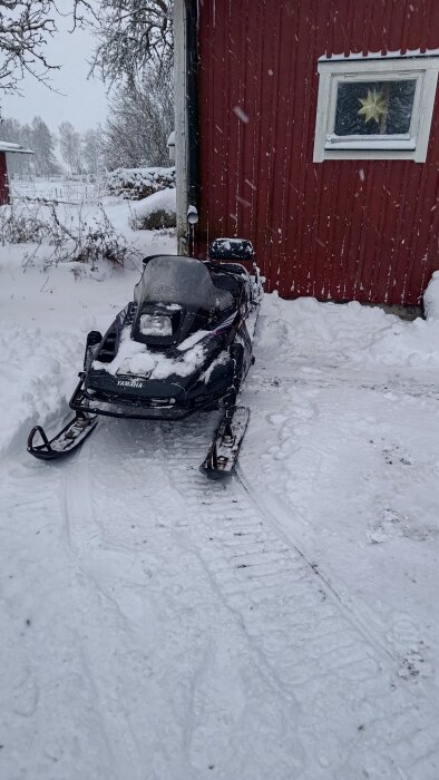 Snöskoter parkerad vid en röd byggnad, omgiven av snö, efter snöröjning och vinteraktiviteter.