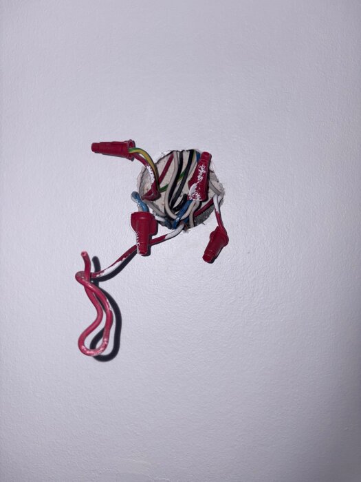 Elkablar synliga från ett vägguttag, med öppnat lock, olika ledare ligger exponerade i en bostad under renovering eller inspektion.