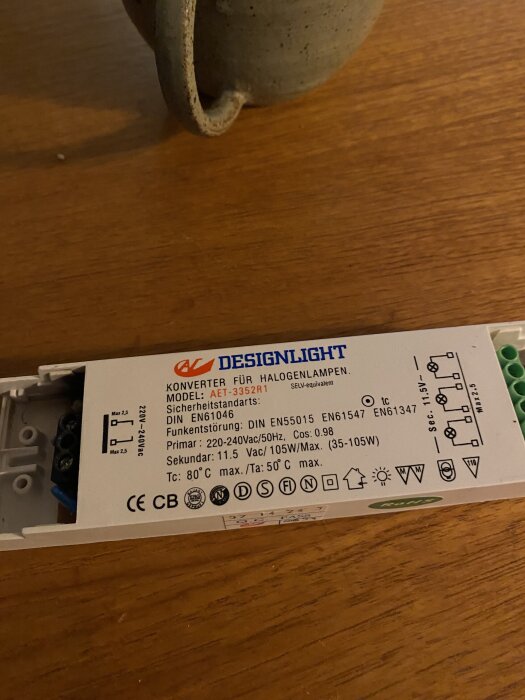 Konverterare för halogenlampa med specifikationer, modell AET-3352R1 från Designlight, liggande på ett bord bredvid en kopp.
