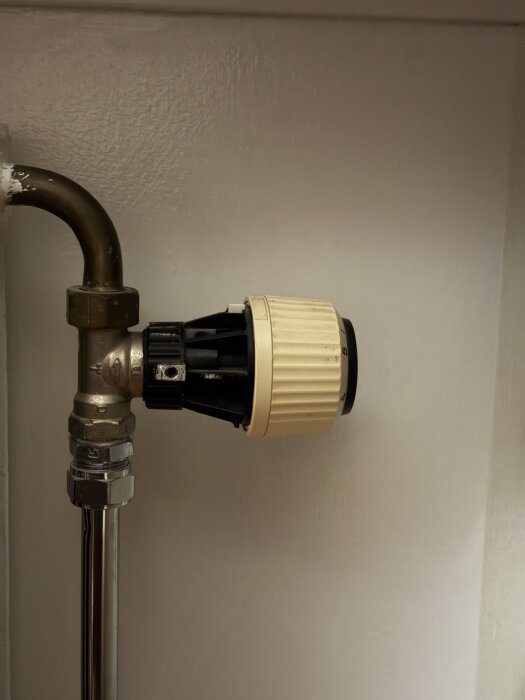 Radiatorventil med termostat monterad på ett kopparrör mot en vit vägg.