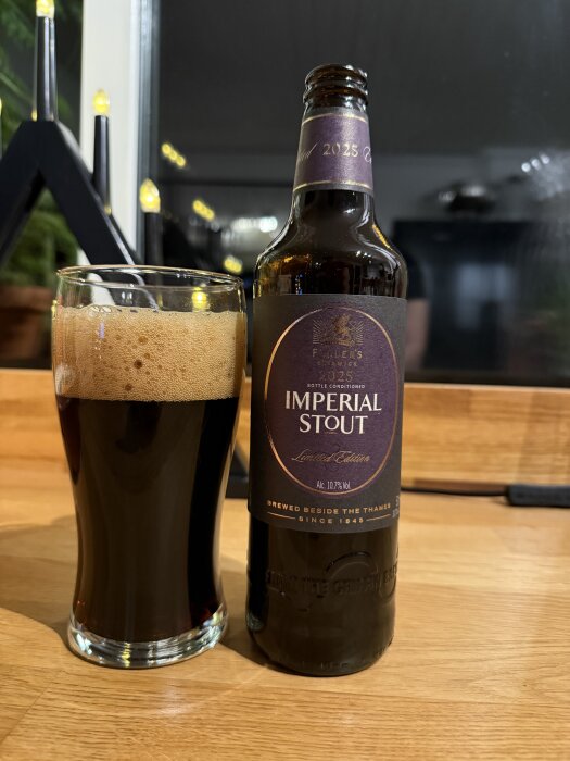 Flaska och glas med mörk Imperial Stout-öl på ett bord, bredvid en tänd ljusstake i bakgrunden.