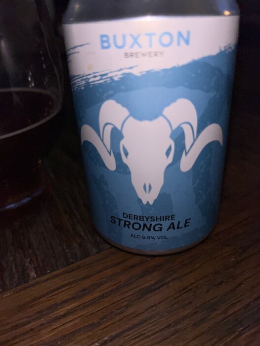 En burk Buxton Strong Ale bredvid ett glas, fotograferad på ett trädäck.