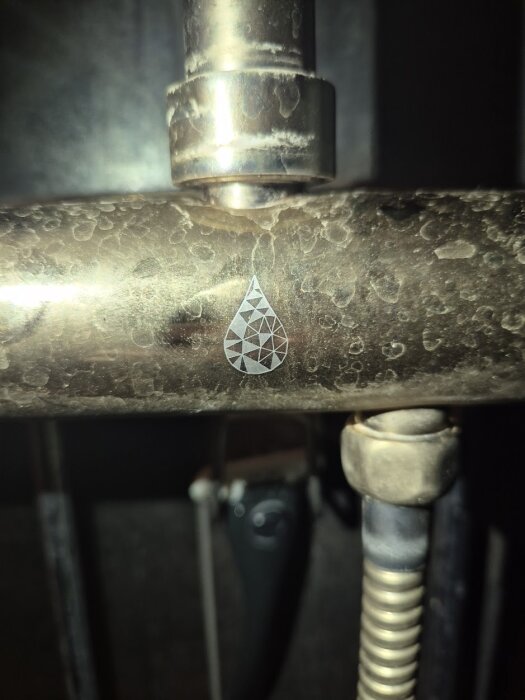 Duschblandare med en geometrisk droppsymbol på en metallisk yta som visar tecken på kalkavlagringar och slitage.