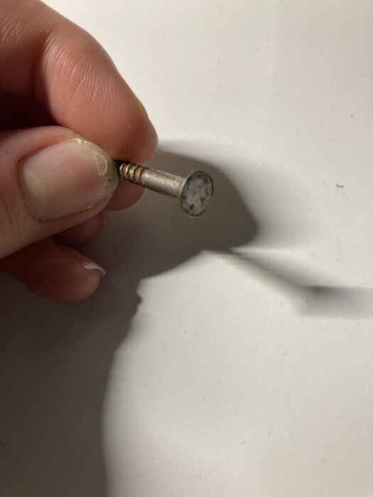 En hand håller en rostig skruv mot en vit bakgrund.