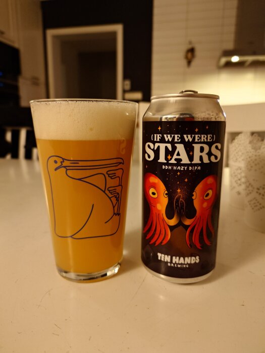 Ett glas hazy DIPA-öl bredvid en ölburk med en bläckfiskdesign från Ten Hands Brewing, på ett köksbord.