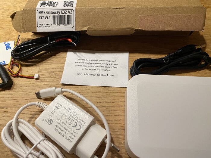 Paket med EMS Gateway E32 V2 kit och tillbehör, inklusive kablar och en nätadapter, placerade på ett bord.