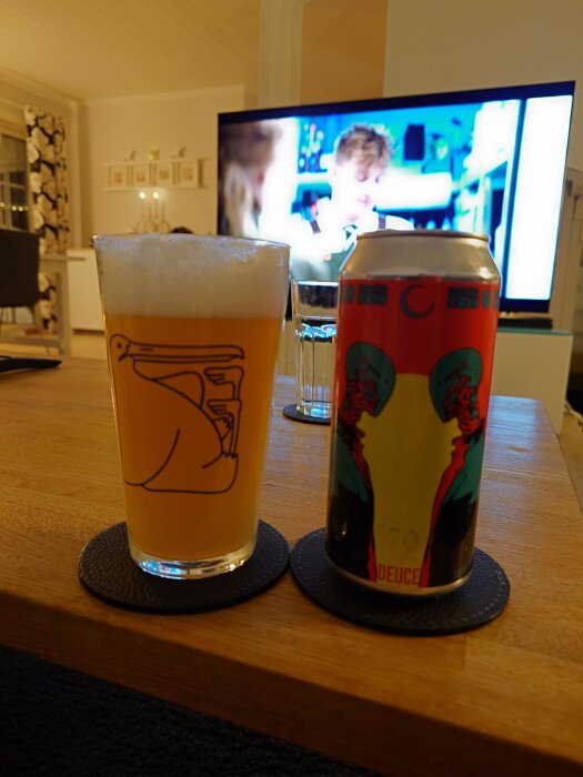 Ett glas öl och en ölburk står på ett bord på glasunderlägg framför en TV. Både glaset och burken har unik grafik.