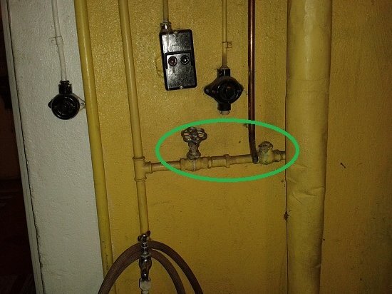 En gammal installation av radiatorpåfyllning med lös avstängningsventil och backventil på gul bakgrundsvägg.