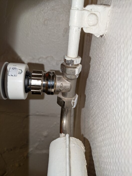 Radiatoranslutning med termostat och rör i en villa. Termostaten är inställd på nivå 6, och rörförbindelserna är inbyggda i väggen.
