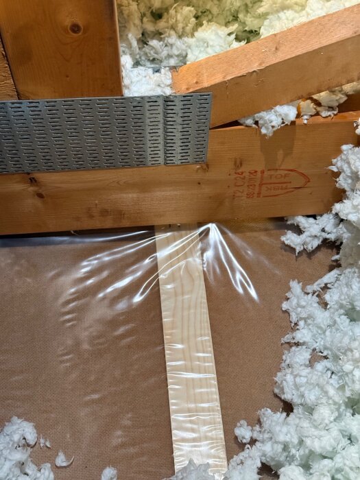 Byggdetalj med träreglar, isolering och metallbeslag i närbild.