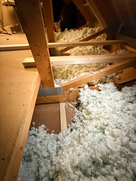 Loftutrymme med synliga bjälkar och isoleringsmaterial, vilket visar konstruktionen av ett bjälklag för ljudisolering.