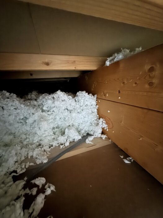 Bjälklag med träreglar och isoleringsmaterial i form av vit fluffig cellulosafiber, sett från sidan under ett golv.