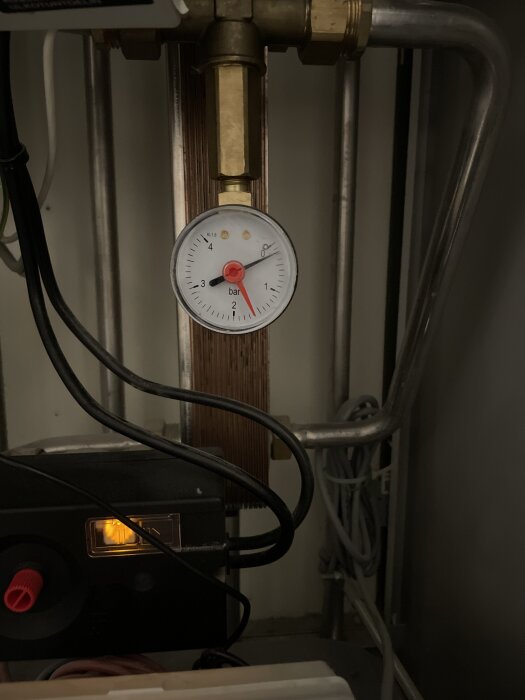 Manometer vid elementets röranslutning visar tryck, omgiven av ledningar och ventiler, som en del av husets värmesystem.