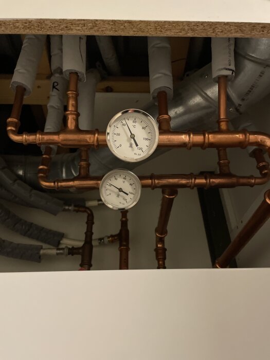 Kopparrör med två termometrar i en husinstallation, del av ett värmesystem som inte fungerar korrekt.