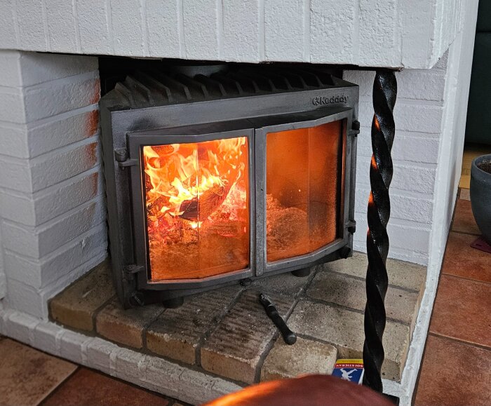 Brasa brinnande i en tegelöppen spis med ved inuti, mysig värme inomhus när det är kallt ute.