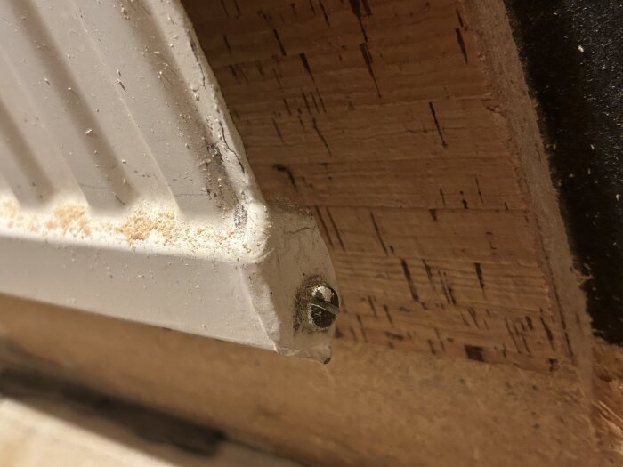 Närbild på en vit radiator ansluten till en vägg av trä, med synlig skruvtipp fastsatt mot träramen.