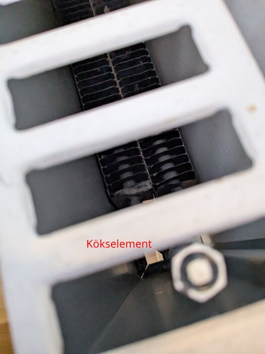 Närbild av rader av metallspjälor i ett värmeelement med etiketten "Kökselement" i röd text.