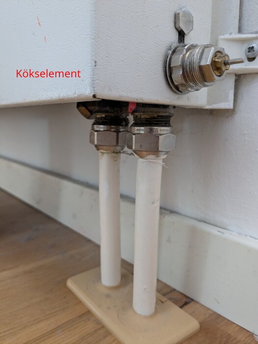 Uppvärmningsrör och ventil vid ett kökselement i ett hem, med mässing och röranslutningar under ett element på ett trägolv.