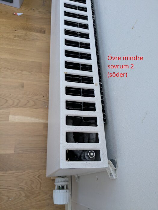 Element i sovrum, ovanvåning, sett från sidan. Detalj av rör och termostat, ljusgrå färg. Text på väggen anger rum: "Övre mindre sovrum 2 (söder)".