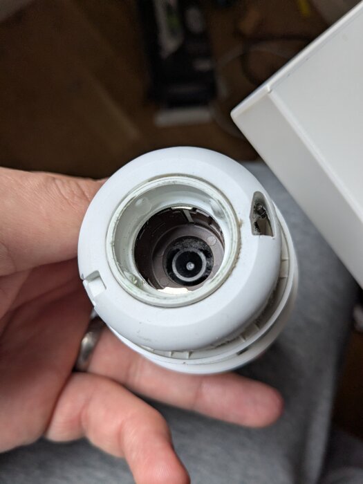 Närbild av en hand som håller en vit termostatventil för radiator, invändig mekanik synlig i centrum.