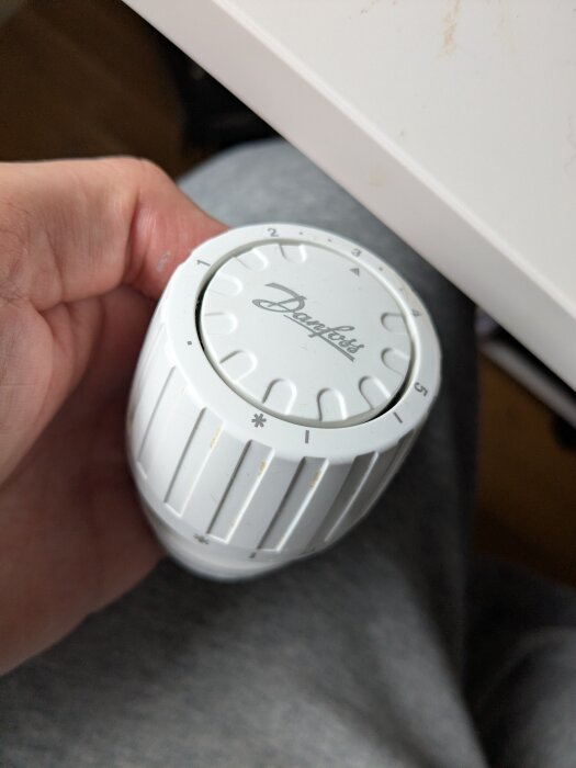 Termostat av märket Danfoss som hålls i handen, sifferskalan synlig, använd för justering av elementets värme.